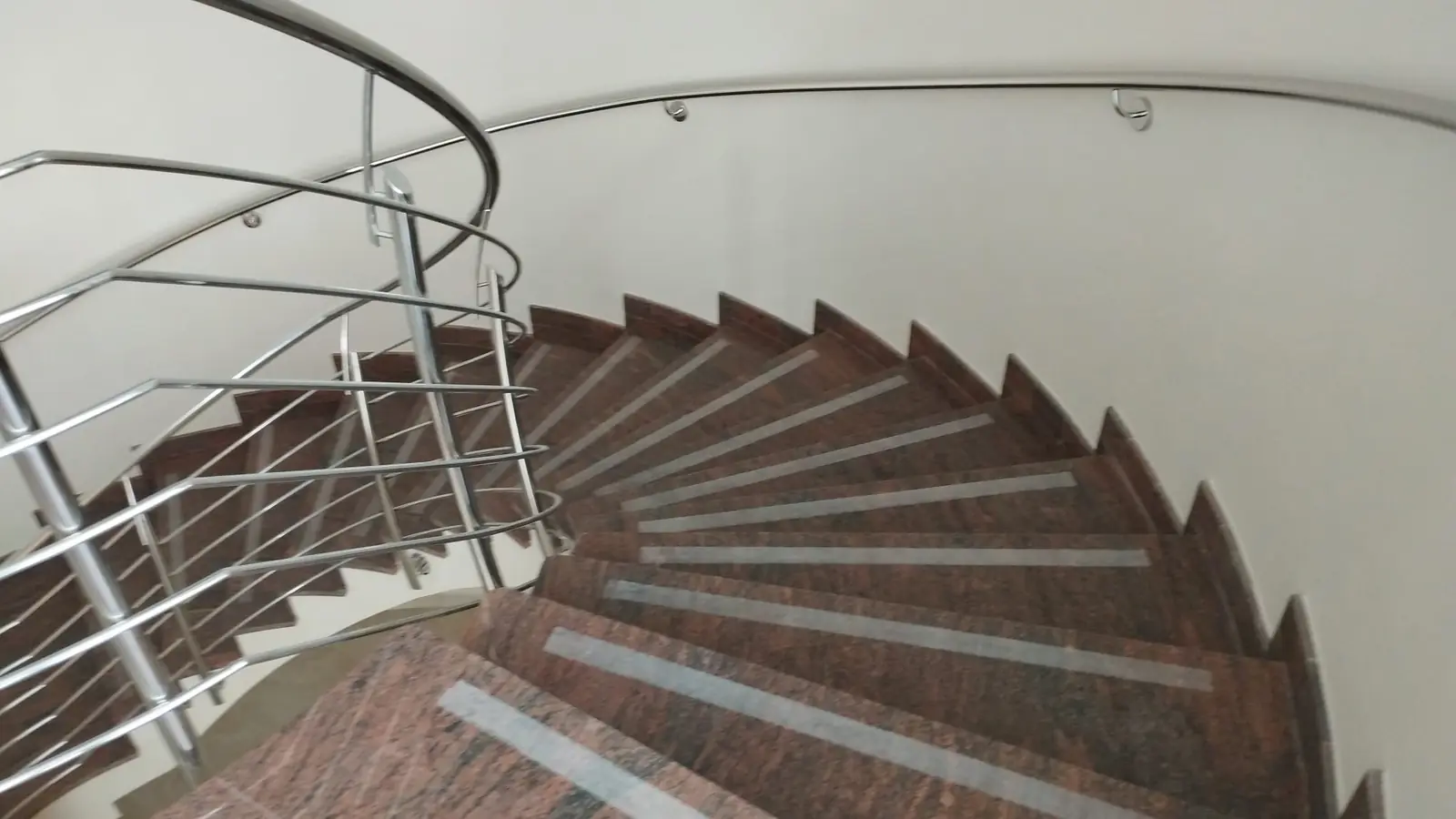 Kręcone schody wewnętrzne z brązowego kamienia i stalową balustradą